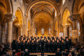 Choir dressed in black robes singing in a cathedral with stained glass windows and gothic arches