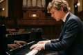 Young man in suit playing grand piano with sheet music in concert hall