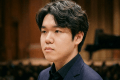 Young man playing a Steinway grand piano on stage in a formal concert venue