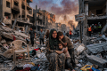 Mother and two children amid rubble; sign reads Al-Shuja'iya District
