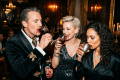 Three formally dressed guests drinking red wine at a candlelit gothic party