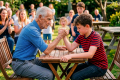 Grandfather and boy arm wrestling at a picnic table while family watches